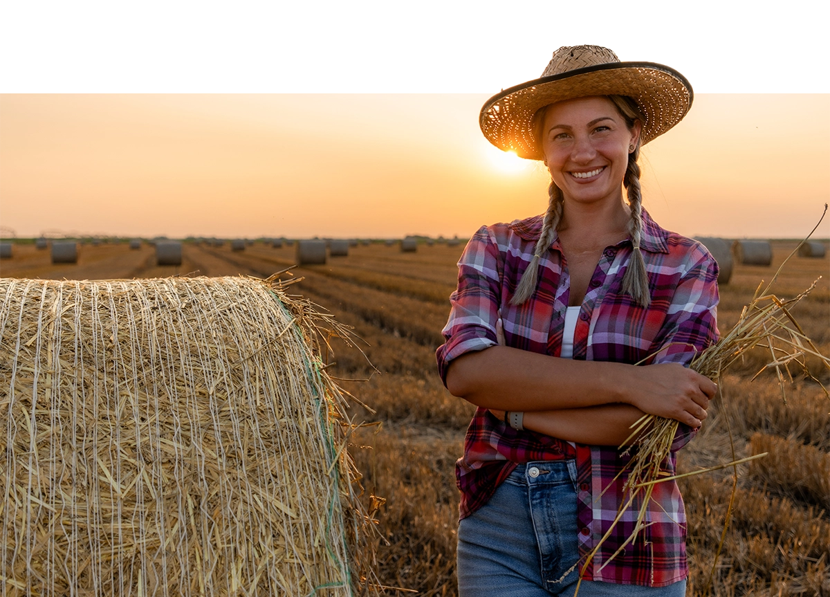 a woman in a straw hat standing in a field with hay bales